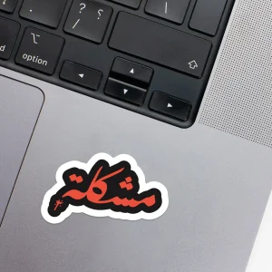 Vinyl Laptop Sticker irregular arabic text moshkela shape with white 3mm outline round corner and orange black text on macbook beside keyboard