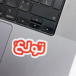 Vinyl Laptop Sticker irregular arabic text tewlaa shape with white 3mm outline round corner and orange text on macbook beside keyboard