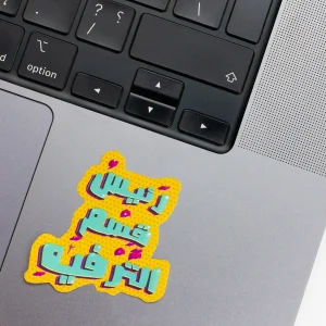 Vinyl Laptop Sticker irregular arabic text raees qesm altarfeeh shape with yellow mustard 3mm outline round corner and cyan blue pink text on macbook beside keyboard
