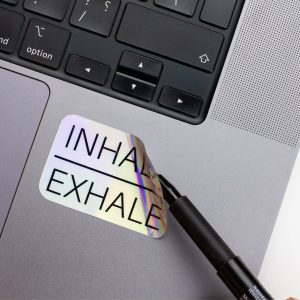 Holographic Laptop Sticker rectangle shape with round corner with black text Inhale Exhale on a macbook corner laptop and top of sticker is removed with a black pen with inner fill shiny metallic rainbow effect