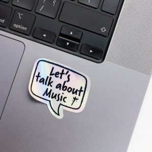 Holographic Laptop Sticker rectangle shape with round corner with black text lets talk about music on macbook beside keyboard peeled off with inner fill shiny metallic rainbow effect