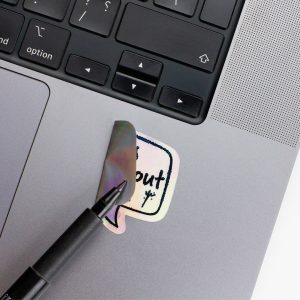 Holographic Laptop Sticker rectangle shape with round corner with black text lets talk about music on macbook beside keyboard peeled off using a black marker with inner fill shiny metallic rainbow effect