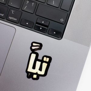Holographic Laptop Sticker irregular arabic text tabban shape with round corner with black text on macbook beside keyboard with inner fill shiny metallic rainbow effect