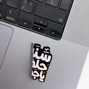 Holographic Laptop Sticker irregular arabic text sanna helwa shape with round corner with black text on macbook beside keyboard with inner fill shiny metallic rainbow effect peeled