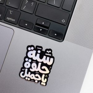 Holographic Laptop Sticker irregular arabic text sanna helwa shape with round corner with black text on macbook beside keyboard with inner fill shiny metallic rainbow effect